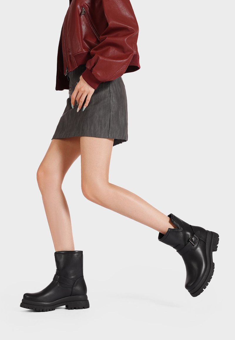 Stivali alla caviglia in pelle nera con punta rotonda e suola spessa. Presentano un dettaglio a fascia attorno alla caviglia e una superficie testurizzata.