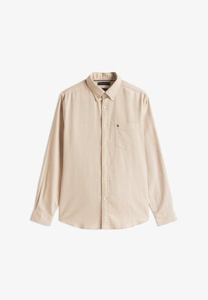 Camicia beige a maniche lunghe in un tessuto morbido con colletto a bottoni, dotata di taschino sul petto e dettagli di texture discreti.