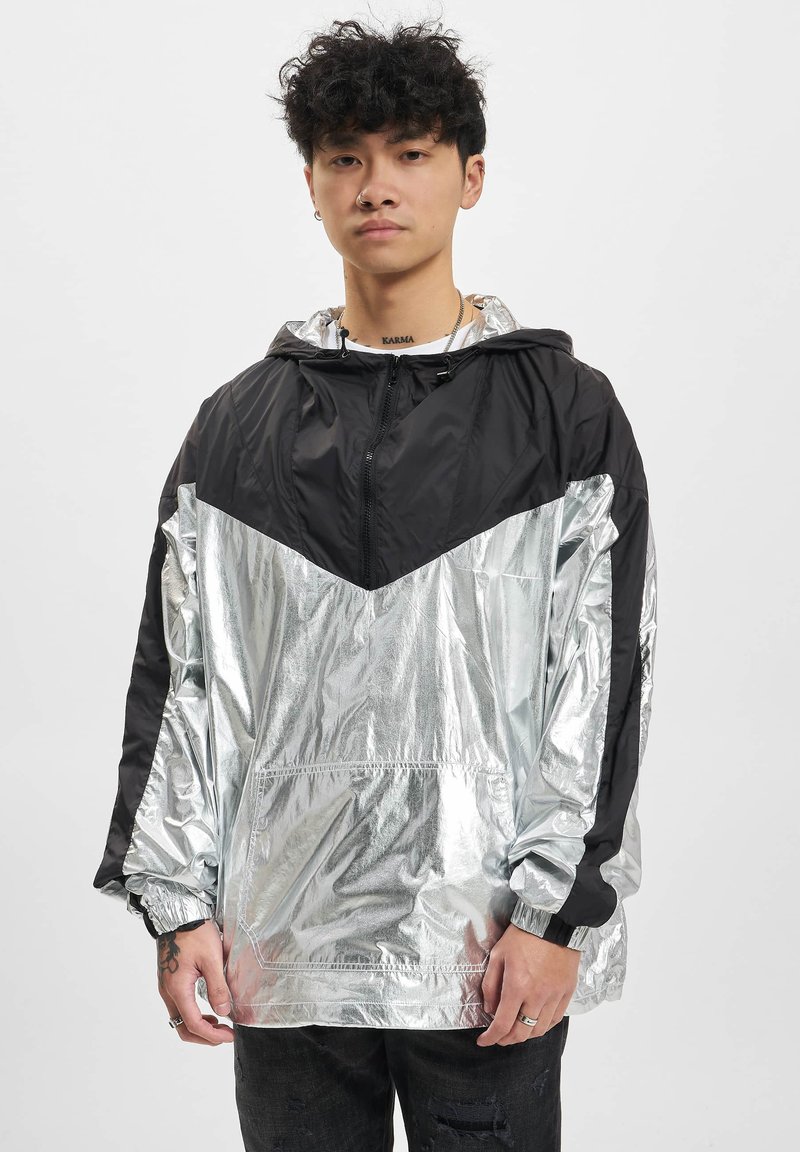 Silberne und schwarze Kapuzenwindjacke mit einem eleganten, glänzenden Finish, ausgestattet mit einem Reißverschluss vorne, elastischen Bündchen und einem diagonalen Farbblockdesign.