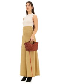 Borsa a tracolla marrone imbottita con parte superiore curva e manici corti, abbinata a una canotta crema aderente e pantaloni beige a vita alta e larghi con dettagli rossi.