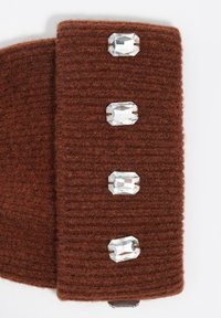 Textil de lana marrón con textura acanalada, con cuatro gemas transparentes facetadas y rectangulares incrustadas a lo largo de un borde.