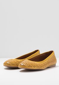 Bailarinas de cuero amarillo con patrón floral recortado, puntera redondeada y suela plana. Textura suave, diseño minimalista adecuado para ocasiones casuales.