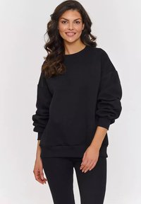 Czarna bluza crewneck z prążkowanymi mankietami i dołem, o luźnym kroju i miękkiej fakturze, w zestawie z pasującymi prążkowanymi legginsami.
