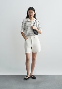 Biała dzianinowa koszulka polo w poziome czarne paski, zestawiona z białymi szortami do kolan i czarnymi szpiczastymi balerinami; mała czarna torebka.