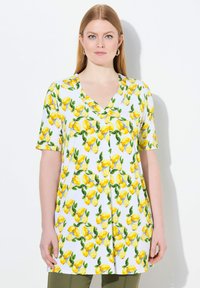 Tunika a maniche corte in tessuto bianco decorato con limoni gialli e foglie verdi, design a V e vestibilità ampia e rilassata.