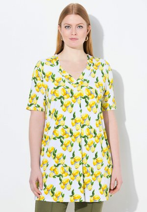 Tunika a maniche corte in tessuto bianco decorato con limoni gialli e foglie verdi, design a V e vestibilità ampia e rilassata.