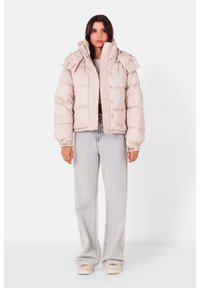 Puffet beige jakke med ribbet tekstur, høj krave og flæse detaljer. Bæres med lyse denim og pastelfarvede sko.