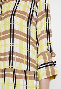 Gelbes und weißes kariertes Kleid mit braunen und schwarzen Streifen, strukturiertem Stoff und einem geknöpften 3/4-Ärmel mit gerafftem Saum.