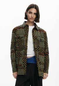 Mønstret jakke med en blanding af houndstooth- og zebra-print i grøn, sort, orange og gul. Har to brystlommer og et krave-design.