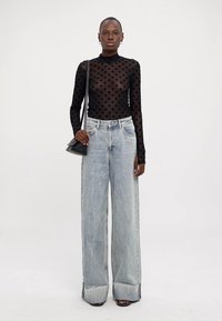 Top negro transparente de manga larga con patrón de diamantes, combinado con unos jeans desgastados de pierna ancha en azul claro y un pequeño bolso negro de hombro.