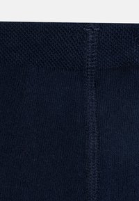 Temno modra pletenina z gladko teksturo in rebrastimi detajli. Šiv viden na sredini za konstrukcijo.