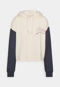 Hoodie cropped in crema con maniche blu scuro. Presenta coulisse, logo ricamato e un tessuto morbido e testurizzato.