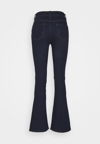 Tmavě modré zvonové džíny s zadními kapsami a poutky na opasek, zobrazené zezadu na jednobarevném bílém pozadí.