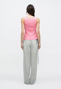 Camiseta de tirantes rosa con textura acanalada y cuello redondo, combinada con pantalones vaqueros grises sueltos que presentan un detalle de cordón en la cintura.