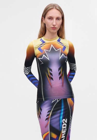 Jeune femme aux longs cheveux blonds portant un haut à manches longues coloré et à motifs, ainsi qu'une jupe assortie avec des formes abstraites et du texte sur la jupe.