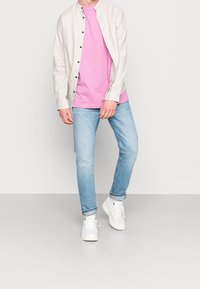 Rento asukokonaisuus, jossa on vaalean beige nappipaita, vaaleanpunainen T-paita, vaaleansiniset farkut ja valkoiset lenkkarit. Yksinkertainen muotoilu ja värimaailma.