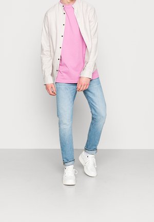 Neformální outfit sestávající z lehce béžové košile na knoflíky, růžového trička, světle modrých džín a bílých tenisek. Jednoduchý design a barevné schéma.