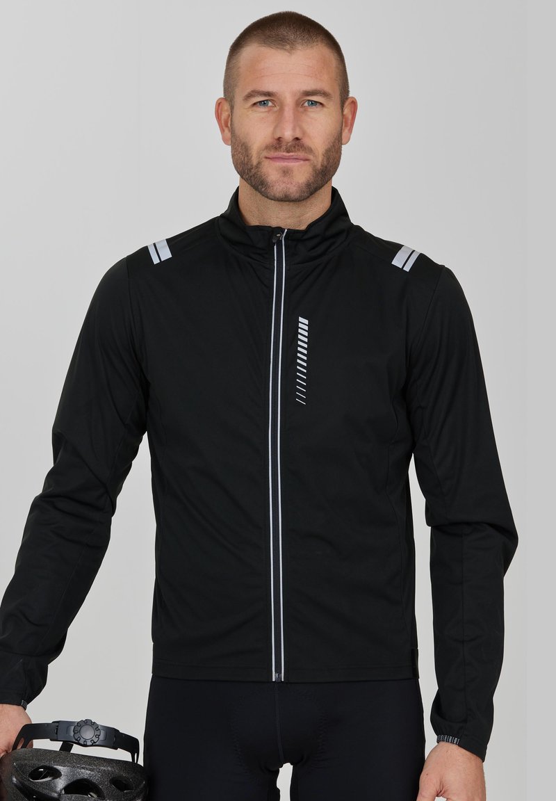 Svart cykeljacka med dragkedja framtill, med reflexstripes på axlarna och ett vertikalt mönster på bröstet. Lättviktigt material.