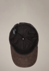 Brązowa czapka z miękkim, zamszowym rondem i ciemną, materiałową wyściółką wewnątrz. Na koronie widoczny jest przeszywany wzór oraz mały metalowy guzik na szczycie.