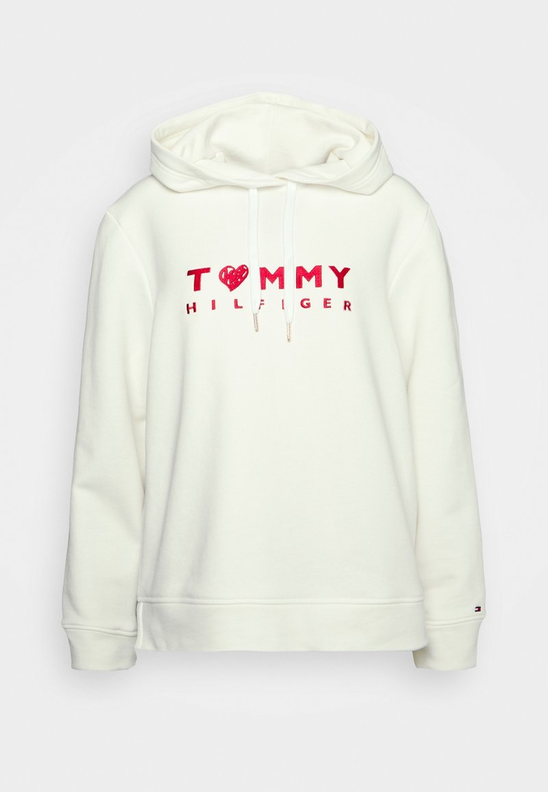 Sweat à capuche blanc avec texte rouge "TOMMY HILFIGER", symbole cœur remplaçant le "O", cordons et petit logo sur le poignet de la manche gauche.