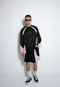 Czarny i różowy strój sportowy z długim rękawem, z prążkowaną teksturą i logo, w zestawie z dopasowanymi szortami i czarnymi trampkami.