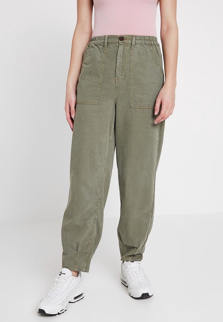 Olive green cargo pants with a relaxed fit, elastic waistband, two front pockets, and cuffed ankles, paired with white sneakers.