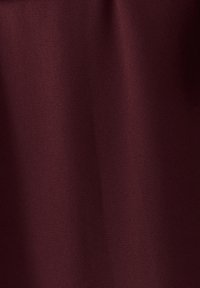 Burgundi audinys su lygiu, tekstūriniu paviršiumi, rodančiu subtilius atspalvių ir šviesos atspindžių pokyčius. Nematyti jokių raštų ar metalinių detalių.