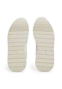 White rubber sneaker soles with horizontal grooves, textured patterns, and embossed "TOMMY JEANS" lettering.