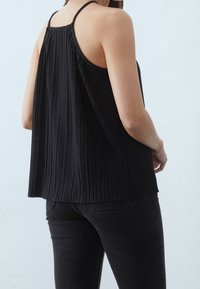 Débardeur noir plissé avec des fines bretelles et une coupe ample, doté d'une surface texturée. Porté avec un jean noir, vu de dos.