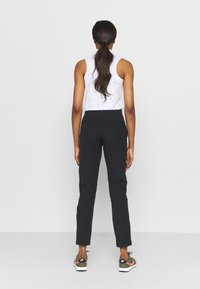 Svarta slim-fit byxor med två bakfickor, kombinerat med en vit ärmlös topp med ett fläckigt mönster, bärs tillsammans med sportiga skor.