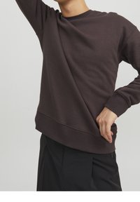 Felpa con colletto rotondo marrone scuro in tessuto morbido e testurizzato, con vestibilità comoda e polsini a costine, abbinata a pantaloni neri.