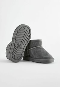 Graue Wildleder-Stiefeletten mit einem weichen Innenfutter und Gummisohlen, die ein Zickzack-Profilmuster aufweisen. Seitliche Nähte akzentuieren das Design.