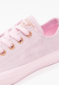 Sneaker in suede rosa con punta rotonda, occhielli beige e suola testurizzata in rosa abbinato. I lacci sono di un rosa chiaro e presentano un'etichetta con logo.