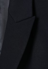 Gros plan sur un tissu bleu marine, présentant une surface texturée et un bord plié, avec de fines rayures horizontales en arrière-plan.