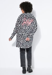 Leopardmønstret jakke med hætte, der har pink "wild" tekst på bagsiden; kombineret med sorte jeans og sort støvler med nitter.