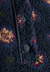 Fleecejacke in Marineblau mit floralen Mustern in Rot-, Lila- und Gelbtönen. Verfügt über schwarze Druckknöpfe und eine strukturierte Oberfläche.