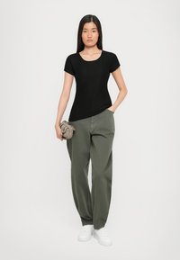 Black ribbed short-sleeve top paired with loose olive-green pants and white sneakers. The model holds a small beige handbag.