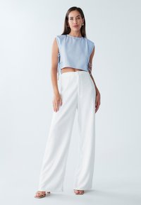 Lysblå cropped top med korte ærmer og sidesløjfer, parret med hvide brede bukser i tekstureret stof. Sandaler fuldender outfittet.