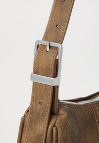Sangle en cuir marron avec une boucle en métal argenté, avec des coutures visibles et une surface texturée. La sangle est ajustable.