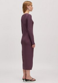 Robe moulante à manches longues en violet profond, fabriquée à partir d'un tissu lisse. Longueur midi, avec un décolleté arrondi et une silhouette ajustée.