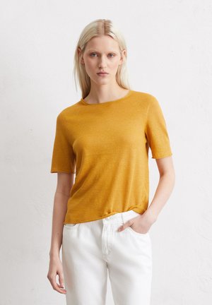 Mosterdkleurig T-shirt met korte mouwen, ronde hals, gemaakt van lichtgewicht materiaal met een lichte textuur, gecombineerd met witte denim jeans.