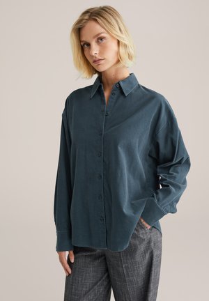 Dark teal button-up shirt with a collar, long sleeves, and a relaxed fit. Soft texture, subtle sheen, and curved hemline enhance design.