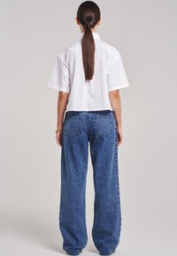 White short-sleeve button-up shirt, paired with loose blue denim jeans. Visible stitching and pockets on the back of the pants.