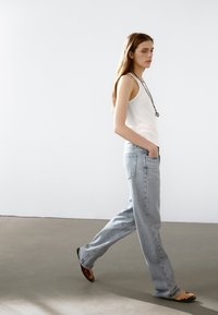Lichtgrijze high-waisted jeans met een rechte snit en een vervaagde afwerking, gecombineerd met een witte tanktop en platte sandalen. Eenvoudige metalen ketting.