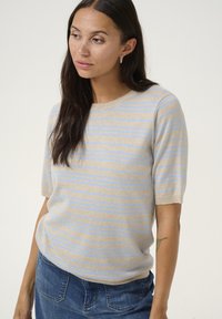 Beżowy sweter z krótkim rękawem w jasnoniebieskie paski, okrągły dekolt, dzianinowa tekstura, w połączeniu z dżinsową spódnicą. Ma luźny krój.
