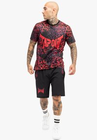 Grafisk atletisk outfit bestående af en rød og sort T-shirt med "TAPOUT" logo og abstrakt design, parret med sorte shorts, som også viser logoet.