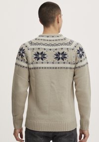 Pull en tricot gris clair avec un motif de flocon de neige en marine et bleu clair, col rond, ourlet côtelé et finition texturée.