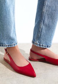 Röda lädersandaletter med spetsiga tår. Ytan är slät med en minimalistisk design och en enskild guldfärgad spänne på remmen.