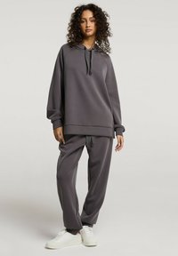 Szara, oversize'owa bluza z kapturem, ściągaczem, prążkowanymi mankietami oraz dopasowanymi luźnymi spodniami, wykonanymi z miękkiego materiału. Białe sneakersy dopełniają zestaw.