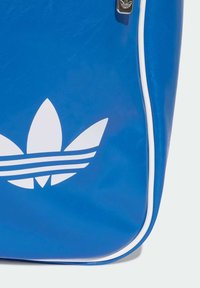 Geantă din vinil albastră cu accente albe. Prezintă un logo mare în formă de trifoi și trei benzi orizontale. Margini rotunjite și elemente de fermoar vizibile.